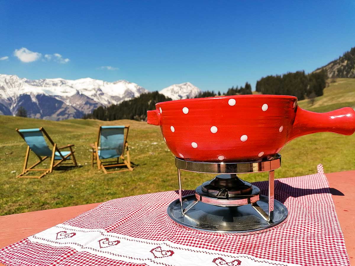 Ein Fondue steht auf dem Tisch vor der Alphütte und mit prächtiger Aussicht auf die Berge.