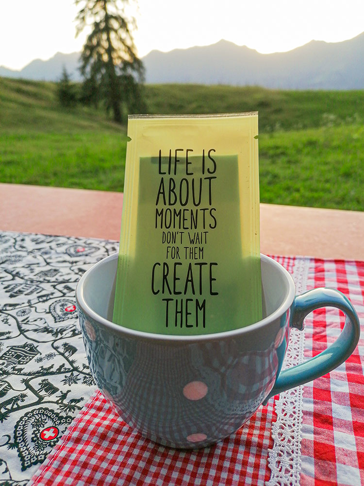 Teetasse auf dem Tisch vor der Alphütte mit Spruch: Life is about moments. Don't wait for them, create them.